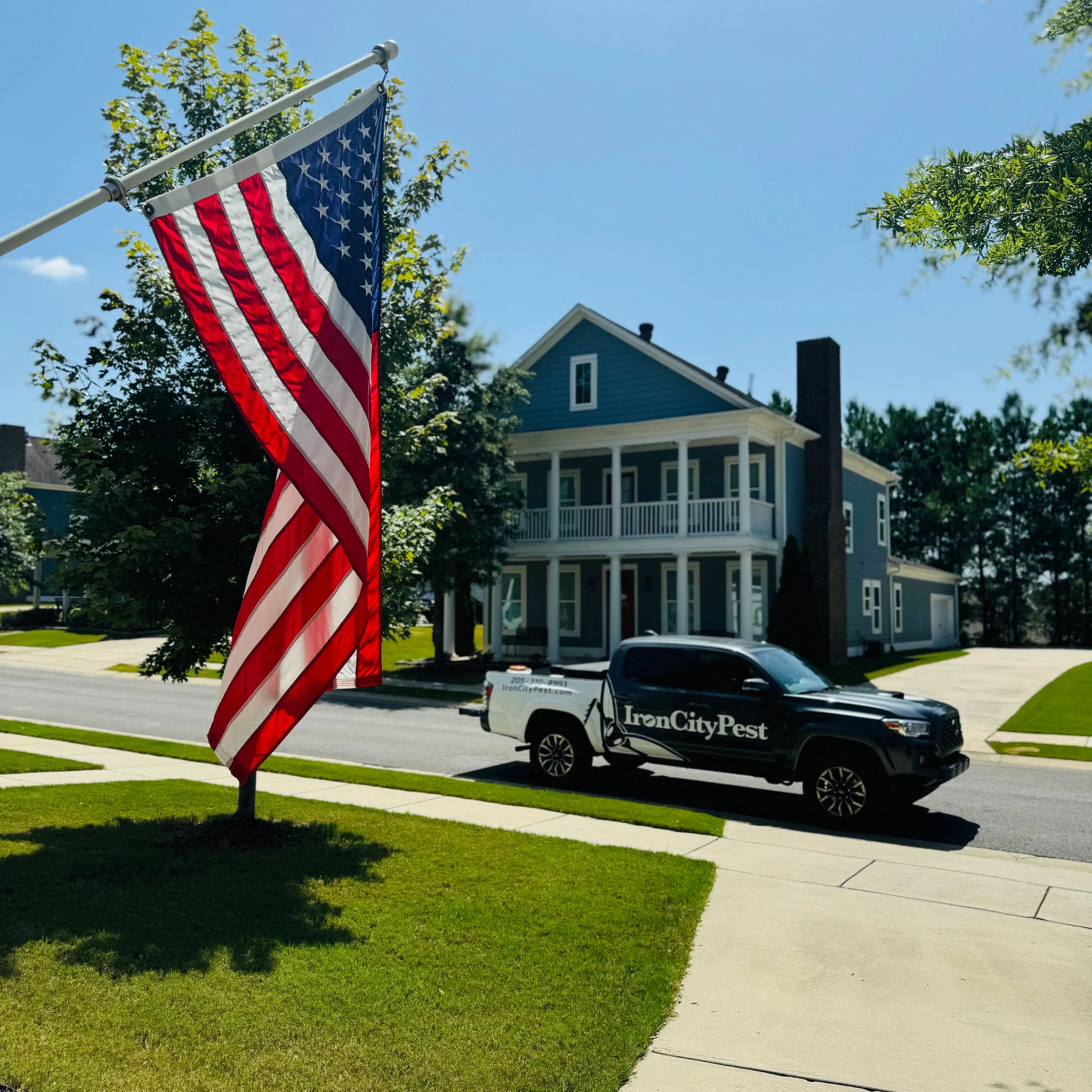 Iron City Pest Management's branded truck parked outside a flag-draped home in a Birmingham-metro neighborhood